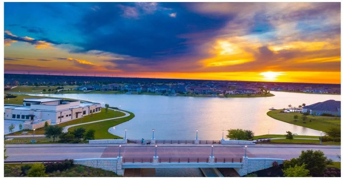 Dramatic orange and blue sunset over a Cypress TX neighborhood with lakeside homes and a modern community center building