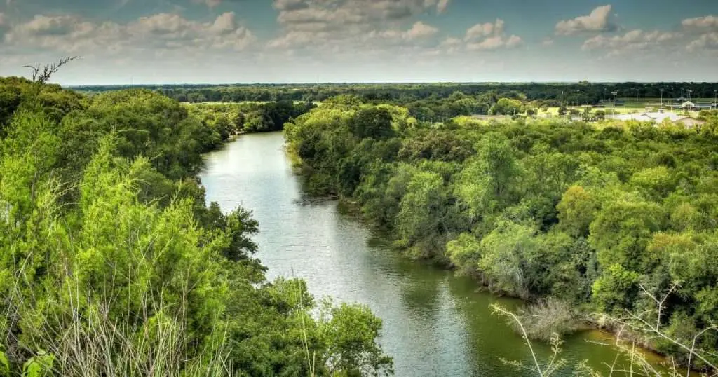 Scenic view of a winding river surrounded by lush green trees and open countryside near Brookshire, Texas.