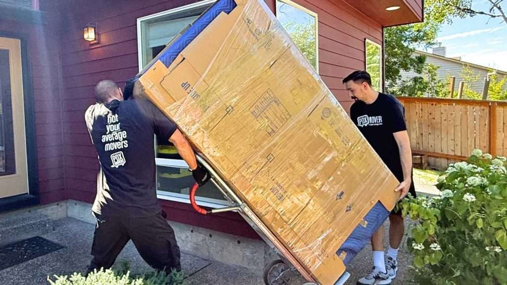 Two Hillboro OR movers hauling wrapped furniture using a dolly
