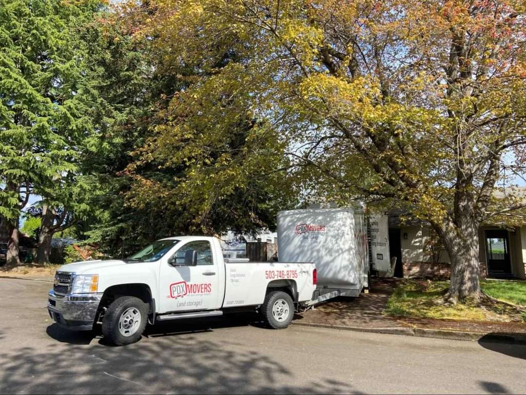 PDX Movers' truck pulling a trailer parked in driveway