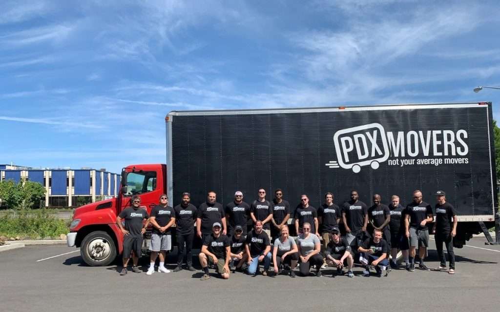 A team of movers poses in front of a moving truck in a parking lot.