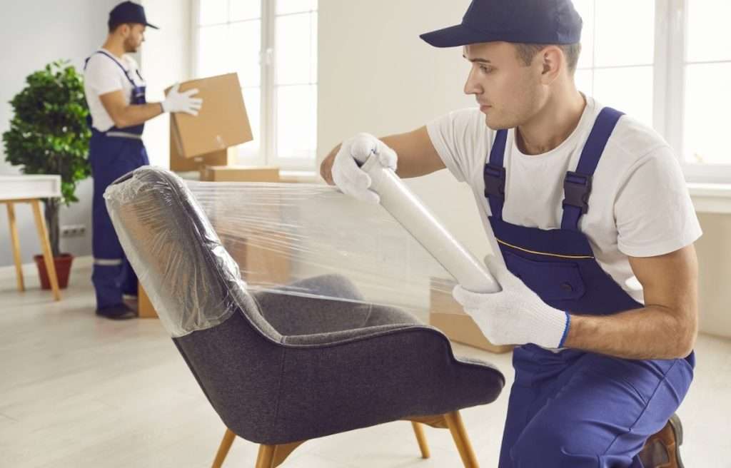 A professional mover wraps an upholstered chair in plastic for protection. 
