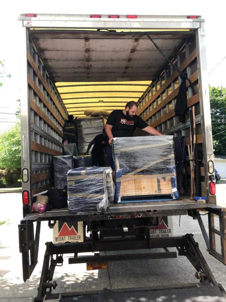 PDX Movers team member unloading wrapped furniture from the back of a moving truck